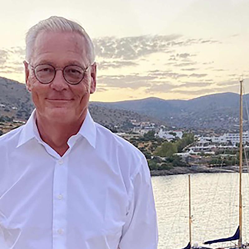Michel, cofounder of Chocolat-e smiles outside in front of a boat yard. Mountains are in the distance.