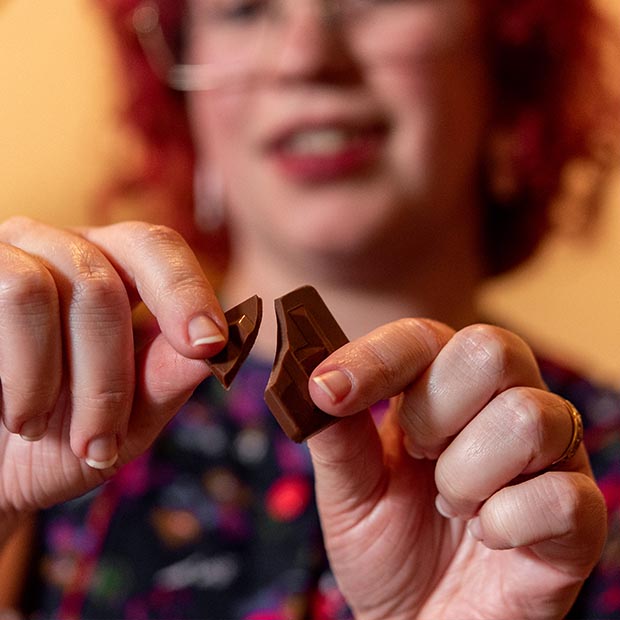 Close up of two hands breaking a piece of Chocolat-e gourmet chocolate. It snaps in the corner.