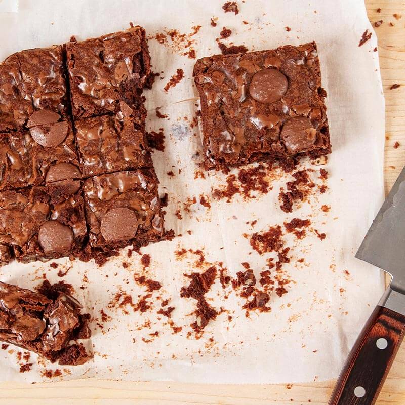 A tray of intense chocolate brownies have been cut into pieces.
