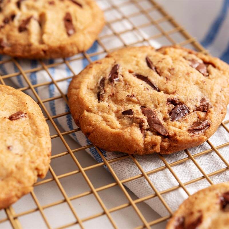 Fresh baked chocolate chip cookies with two types of Chocolat-e single-origin chocolate are on a cooling rack.