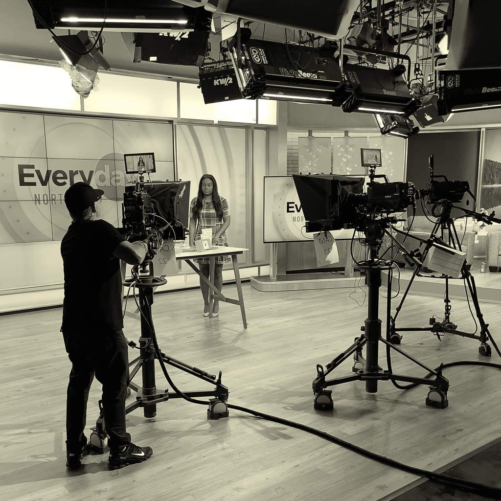 Behind the sceenes at KOIN 6 news. A camera man is recording a reporter who stands behind a table displaying Chocolat-e.