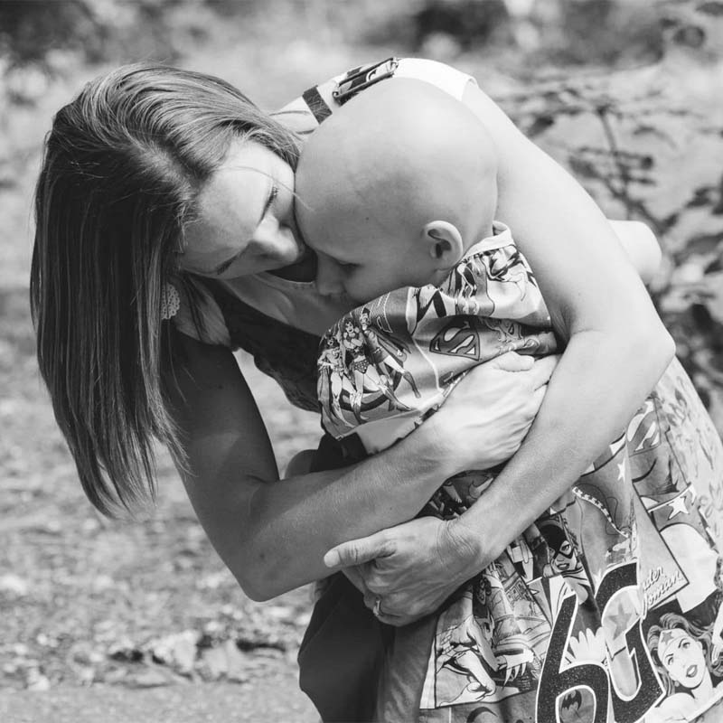 Black and white photo of a person hugging a child who has lost all of their hair.