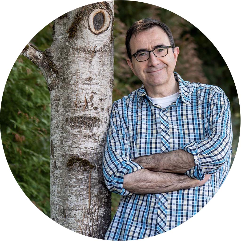 Jeanyves is smiling, leaning against a tree.