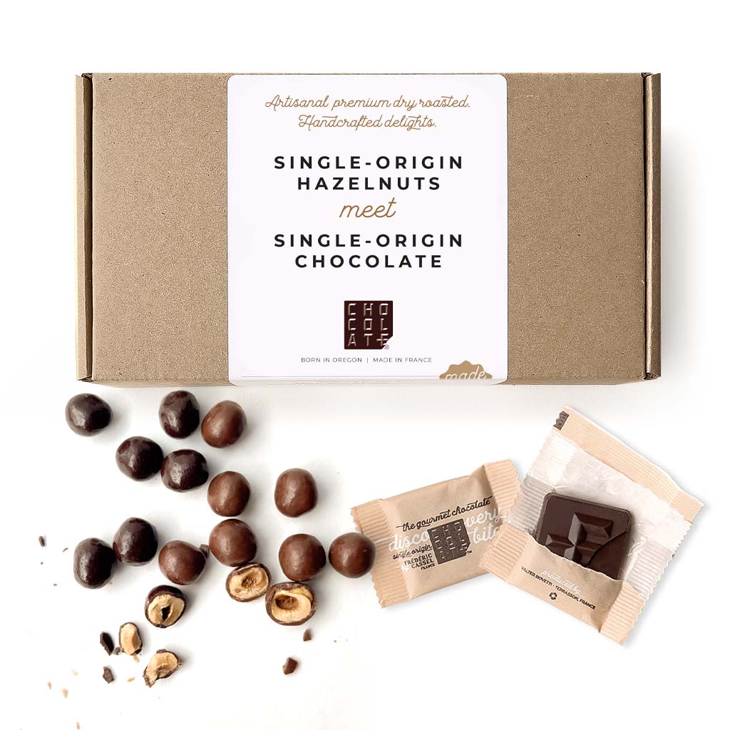 Box of single origin hazelnuts and single-origin chocolates with some loose chocolate covered hazelnuts and Chocolat-e gourmet chocolate bites.