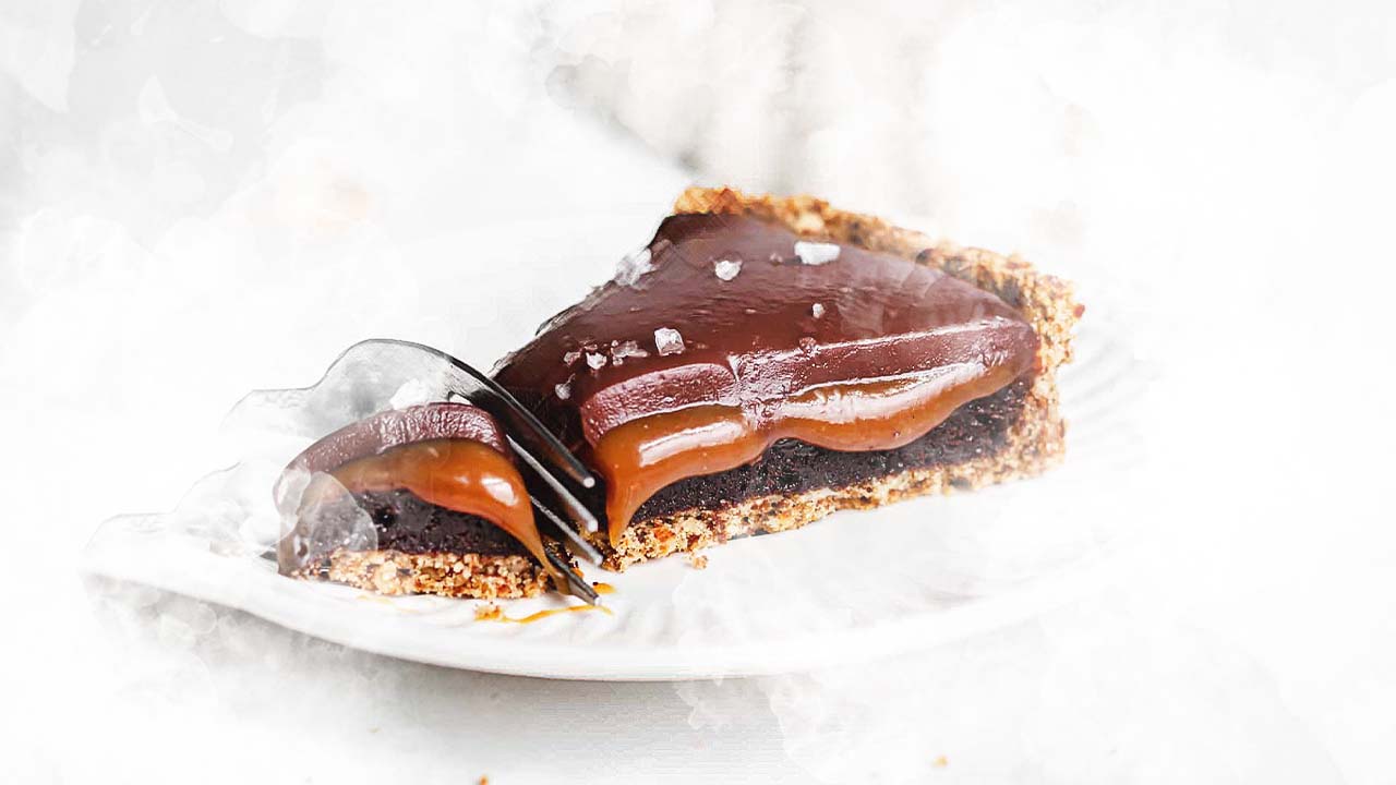 Freshly baked brownies cut by a knife on a cutting board. A bowl of dark chocolate, and dark-milk chocolate baking chips is on the left.